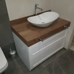 Biała szafka łazienkowa z drewnianym blatem, nablatową umywalką i relingiem na ręczniki, widok z boku.