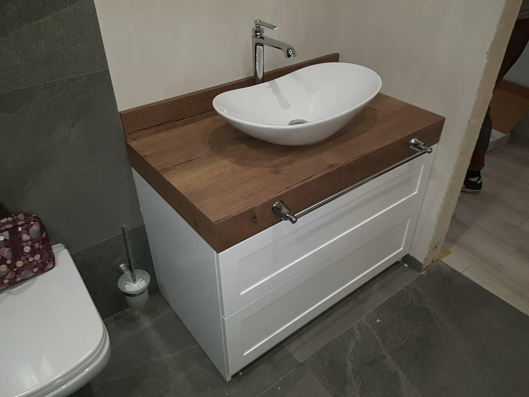 Biała szafka łazienkowa z drewnianym blatem, nablatową umywalką i relingiem na ręczniki, widok z boku.