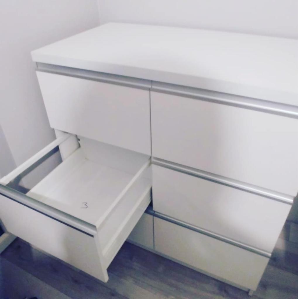 Biała komoda z sześcioma szufladami, z których jedna jest wysunięta, ukazując wnętrze z widoczną cyfrą '3'.