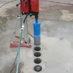 Wiertnica diamentowa Hilti w trakcie wykonywania otworów w betonowej posadzce, widoczne cztery wywiercone otwory i chłodząca je woda.