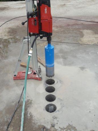 Wiertnica diamentowa Hilti w trakcie wykonywania otworów w betonowej posadzce, widoczne cztery wywiercone otwory i chłodząca je woda.