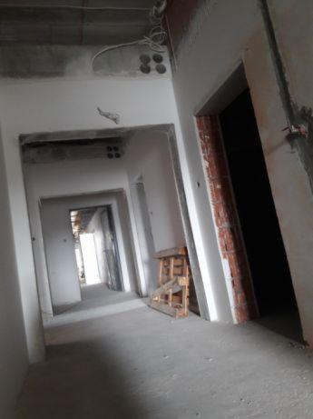 Wnętrze budynku w trakcie rozbiórki ścian, widoczne odsłonięte przewody elektryczne w suficie i fragmenty cegieł wokół otworu drzwiowego.