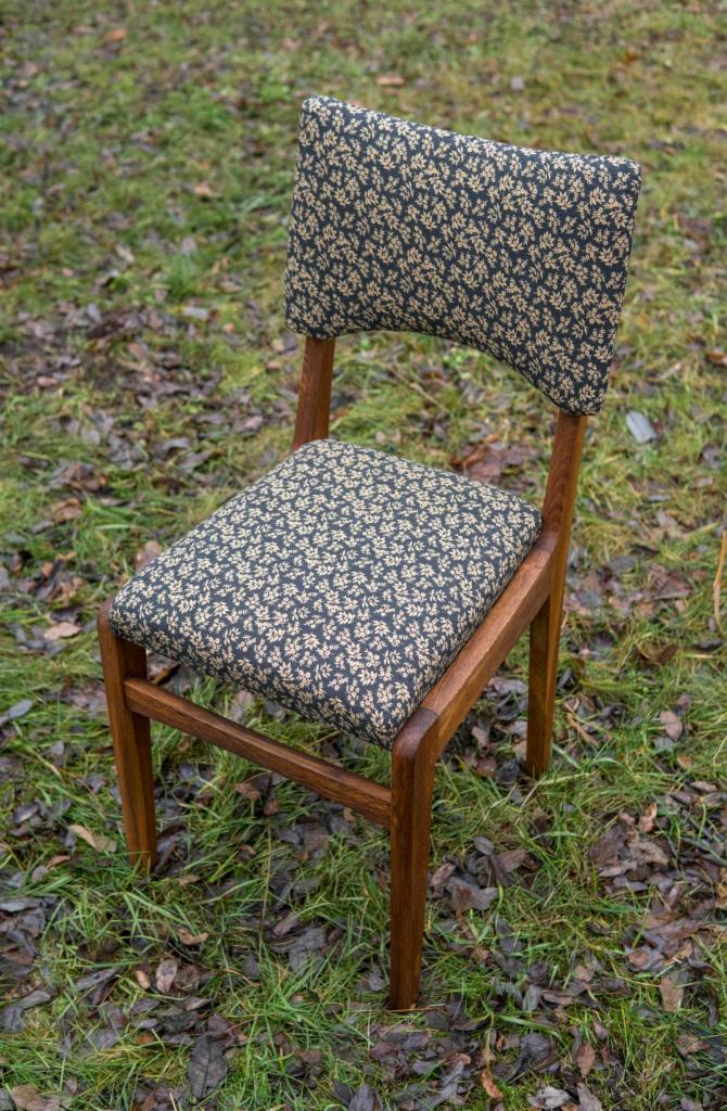 Odnowione krzesło z drewnianą ramą i tapicerką w drobny, beżowo-czarny wzór kwiatowy, ustawione na trawie z liśćmi.