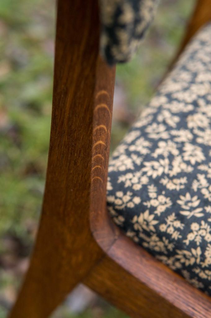 Fragment odnowionego krzesła z ciemnym drewnianym stelażem i obiciem w drobne kwiatki na ciemnym tle, widoczne ślady po renowacji drewna.