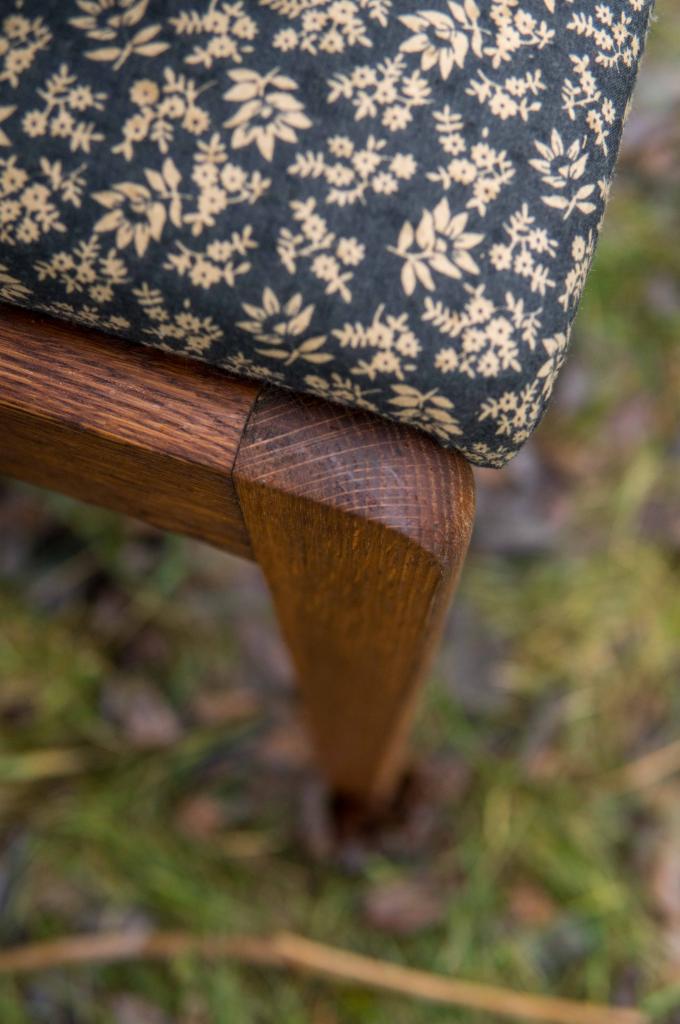 Detale odnowionego krzesła: drewniana noga z widocznym usłojeniem i tapicerowane siedzisko w ciemnym kolorze z drobnym kwiatowym wzorem.