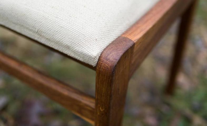 Detale odnowionego krzesła: tapicerowane siedzisko z beżowej tkaniny o wyraźnym splocie, osadzone w ciemnobrązowej, odrestaurowanej drewnianej ramie z widocznymi słojami i zaokrąglonym rogiem.