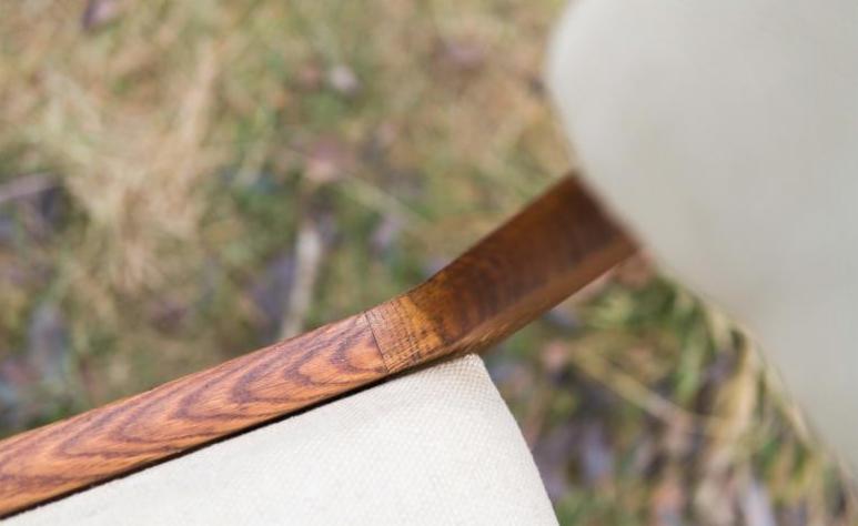 Detal drewnianego podłokietnika krzesła z kremową tapicerką na tle rozmytej zieleni