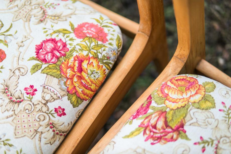 Dwa krzesła z drewnianymi ramami i tapicerką w kwiatowe wzory w odcieniach różu, pomarańczy i zieleni na jasnym tle.