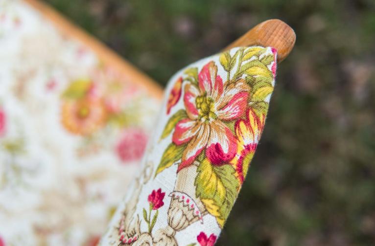 Fragment odnowionego krzesła z drewnianym podłokietnikiem, pokrytego tkaniną w kwiaty i motywy roślinne, widoczne detale wzoru.