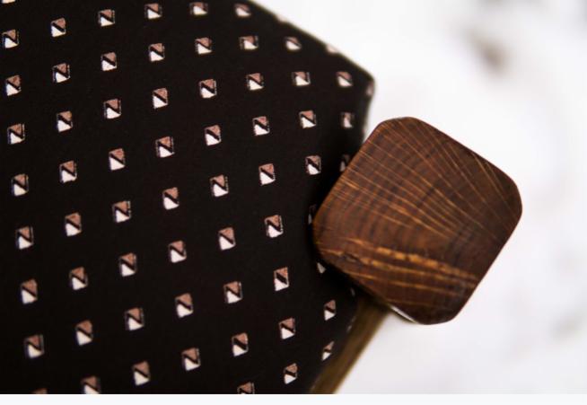 Ciemna tkanina z geometrycznym wzorem małych kwadratów z drewnianym, kwadratowym guzikiem z widocznymi słojami drewna.