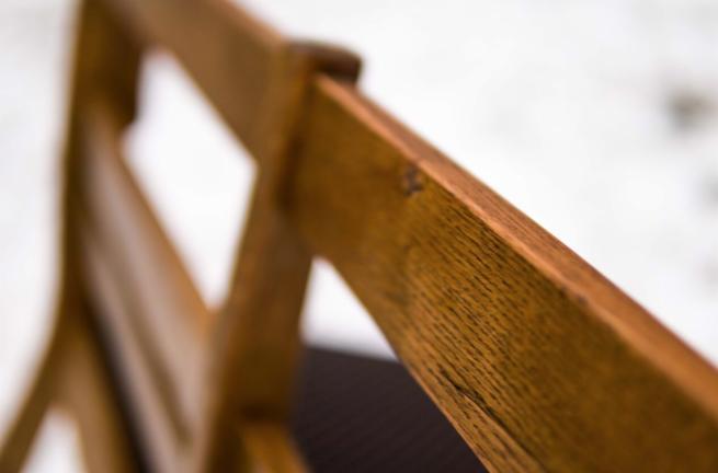 Fragment oparcia krzesła z ciemnego drewna z widoczną strukturą słojów, na rozmytym tle.