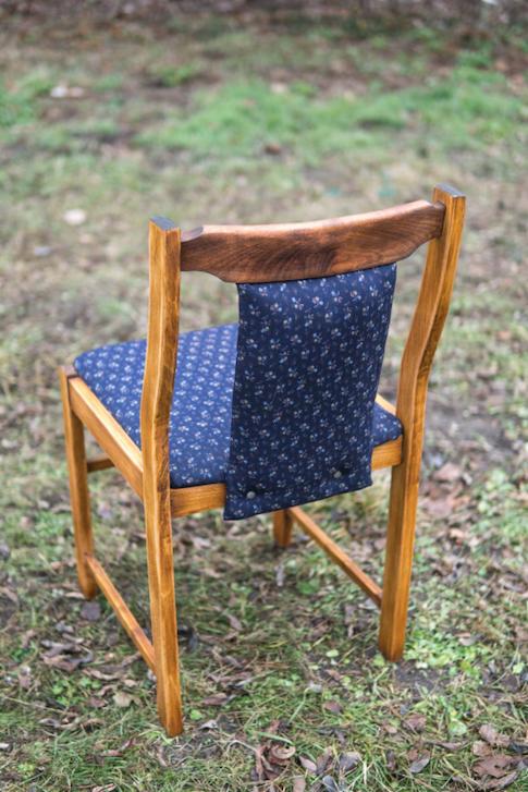 Drewniane krzesło po renowacji z niebieską tapicerką w drobne kwiatki, widoczne od tyłu na tle trawy.