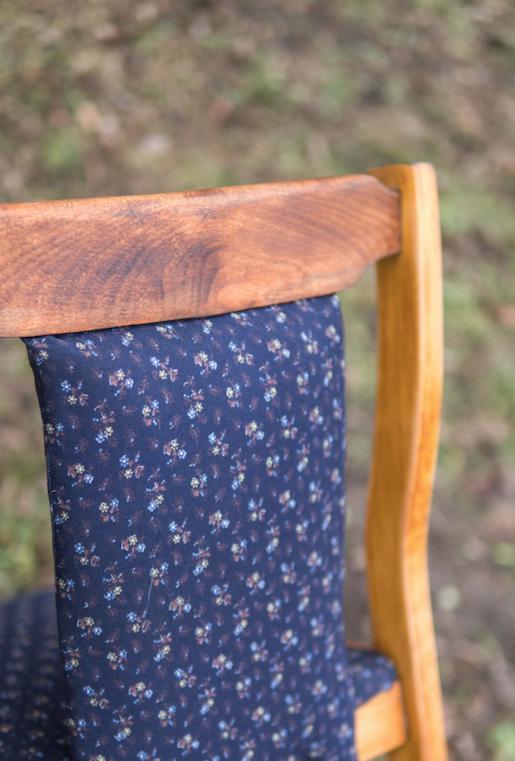 Fragment krzesła z drewnianą ramą i tapicerowanym oparciem w granatowy deseń drobnych kwiatków na tle zieleni.