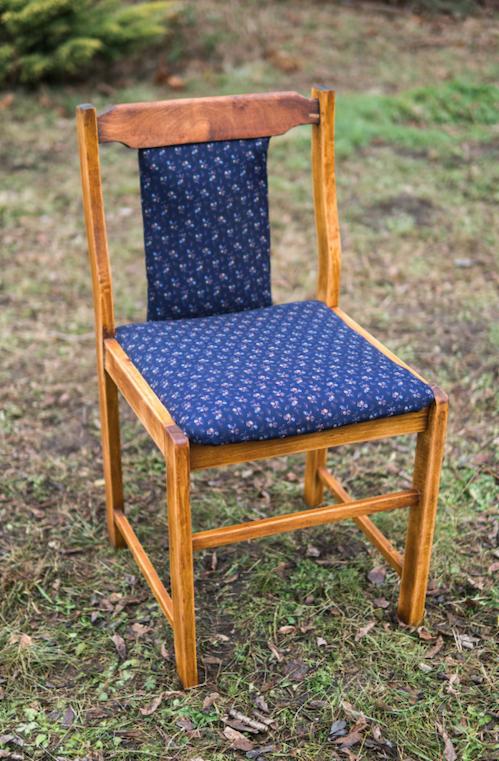 Odnowione krzesło z jasnego drewna z tapicerowanym siedziskiem i oparciem w granatowy wzór kwiatowy, stojące na trawie.