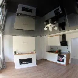 Nowoczesne wnętrze z błyszczącym sufitem, widok na salon z kominkiem elektrycznym i kuchnię z białymi szafkami oraz drewnianymi akcentami, podłoga z paneli imitujących drewno, duże okno z zasłonami