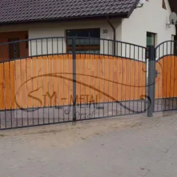 Dwuskrzydłowa brama wjazdowa z metalową ramą i drewnianym wypełnieniem, widoczna z zewnątrz posesji, z numerem domu '30' w tle.