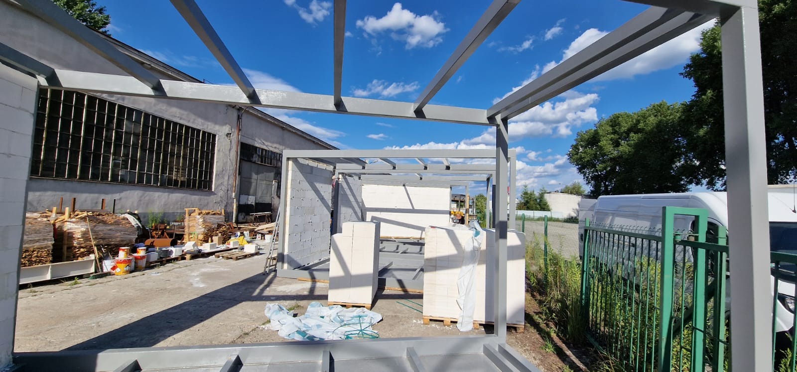 Szkielet domu modułowego z metalową konstrukcją, widoczne ściany z bloczków, materiały budowlane i błękitne niebo w tle.