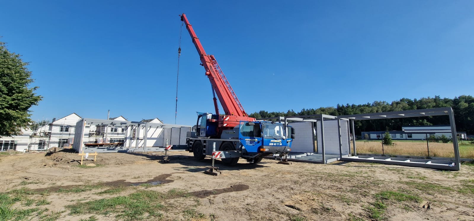 Montaż segmentów domu modułowego za pomocą dźwigu na placu budowy w słoneczny dzień.