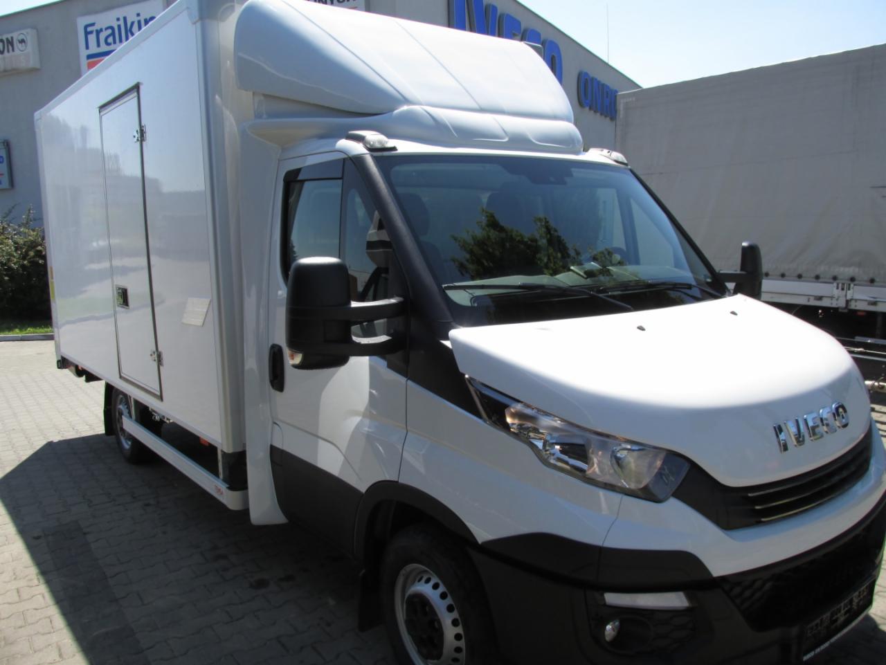 Biały samochód dostawczy Iveco z zabudową kontenerową, widok z boku na tle budynku firmy Fraikim.