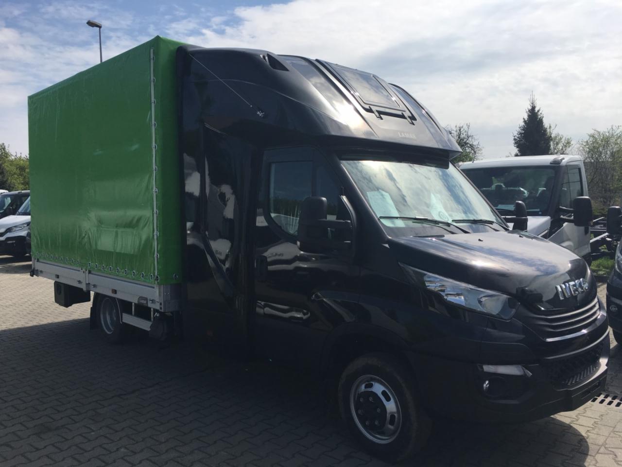 Czarny samochód dostawczy Iveco z zieloną plandeką na parkingu z kostki brukowej, widok z przodu pod kątem.