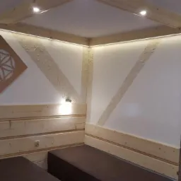 Nowoczesna aranżacja wnętrza sauny z drewnianymi panelami, dekoracyjnym kamieniem na ścianie, oświetleniem LED i geometrycznym ornamentem na ścianie.