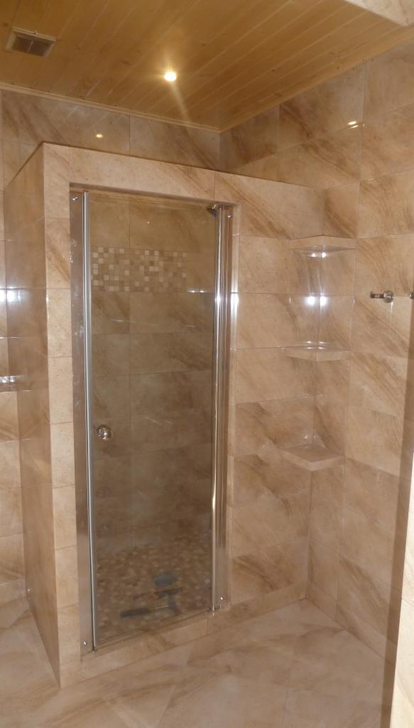 Kabina prysznicowa z przesuwnymi drzwiami w łazience wykończonej płytkami imitującymi marmur, z wbudowanymi półkami.