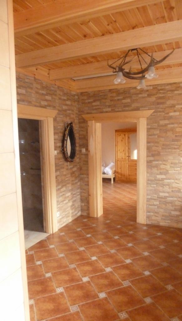 Wnętrze pokoju z drewnianym sufitem, ścianą z kamienia dekoracyjnego, terakotową podłogą i oryginalnym żyrandolem z poroża