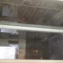 Montaż ramy kabiny prysznicowej z widocznymi punktami mocowania na tle ciemnych płytek w łazience w trakcie prac wykończeniowych.