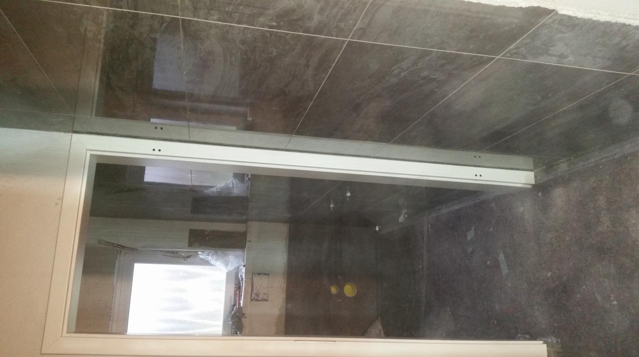 Montaż ramy kabiny prysznicowej z widocznymi punktami mocowania na tle ciemnych płytek w łazience w trakcie prac wykończeniowych.