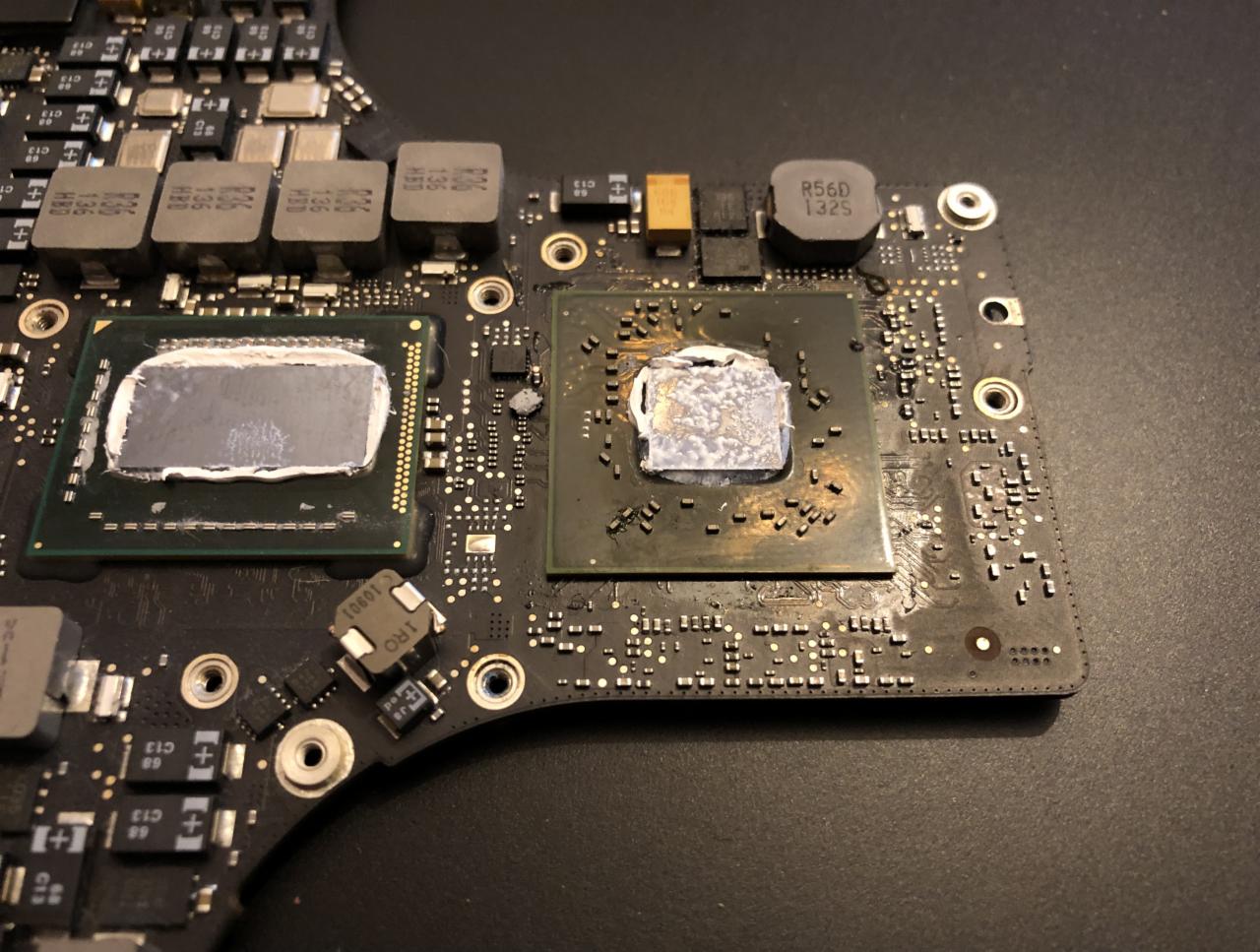 Fragment płyty głównej laptopa z dwoma procesorami pokrytymi pastą termoprzewodzącą, widoczne drobne elementy elektroniczne i oznaczenia na laminacie. Pasta na jednym procesorze wygląda...