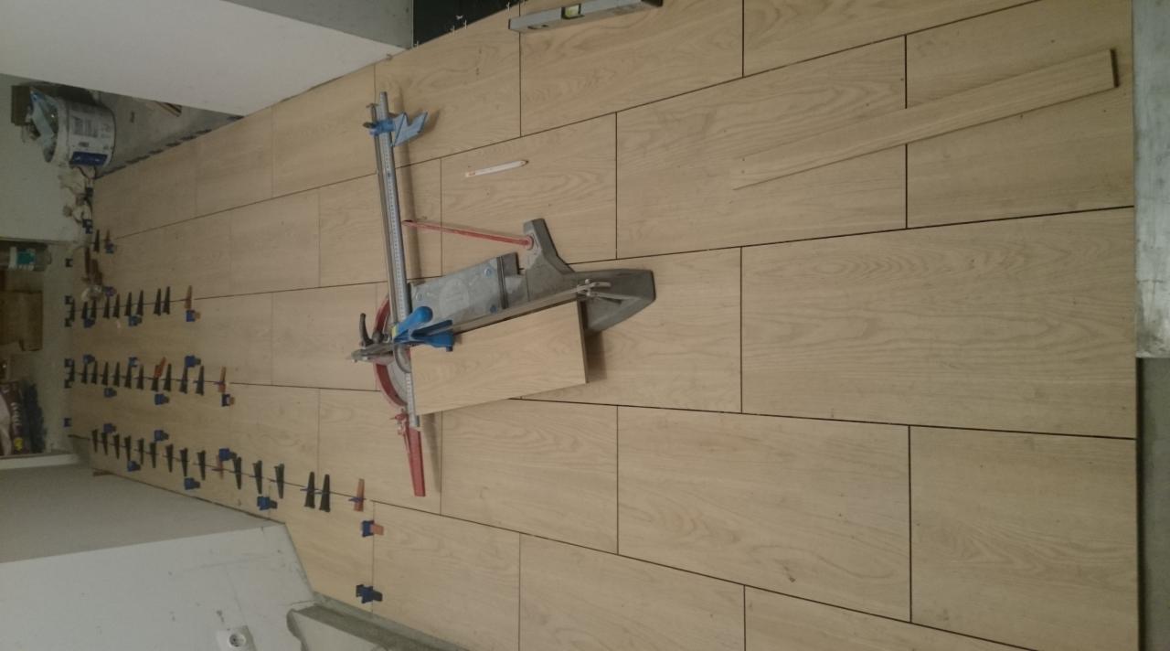 Układanie podłogi z płytek imitujących drewno, widoczny przecinak do płytek i kliny dystansowe.