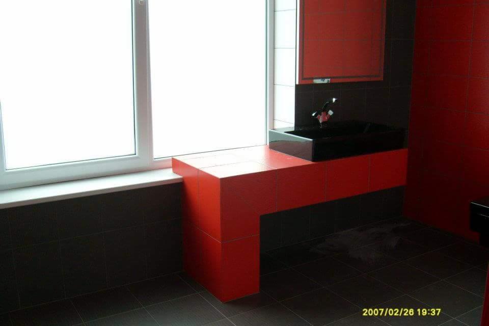 Nowoczesna łazienka w odcieniach czerwieni i grafitu z czarną, prostokątną umywalką nablatową i minimalistyczną baterią, wykończona płytkami z subtelną fakturą.