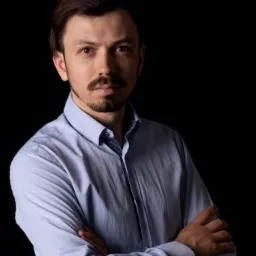 Portret mężczyzny z brodą i wąsami, w błękitnej koszuli, z założonymi rękami na czarnym tle.