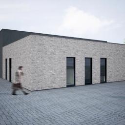 MSDL Michał Szuba Design LAB - Wizualizacja budynku usługowego z szarej cegły i czarnymi panelami, z dwoma rozmytymi postaciami na brukowanym placu przed budynkiem, logo projektanta w prawym dolnym rogu.