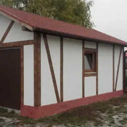 Nowoczesny garaż w stylu szachulcowym z brązową bramą i czerwoną dachówką, otoczony zielenią i lekko ośnieżonym terenem.