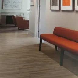 Jasne, drewnopodobne panele na podłodze w nowoczesnym wnętrzu z pomarańczową ławką i obrazami na ścianie.