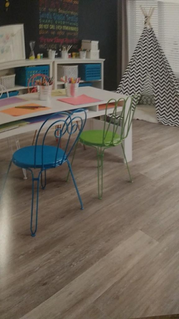 Jasna podłoga panelowa w pokoju dziecięcym z niebieskim i zielonym krzesłem, biurkiem i tipi w tle.