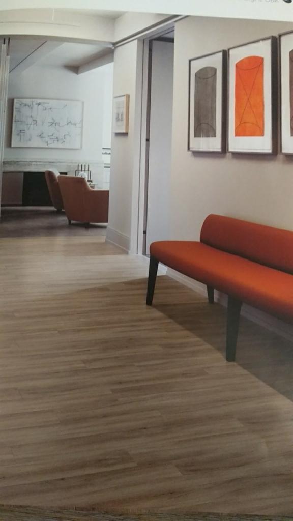 Jasne, drewnopodobne panele na podłodze w nowoczesnym wnętrzu z pomarańczową ławką i obrazami na ścianie.