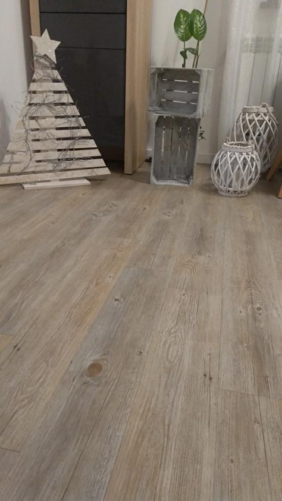 Jasna podłoga z paneli laminowanych o wzorze drewna, w tle drewniana dekoracja świąteczna, skrzynki i lampiony.