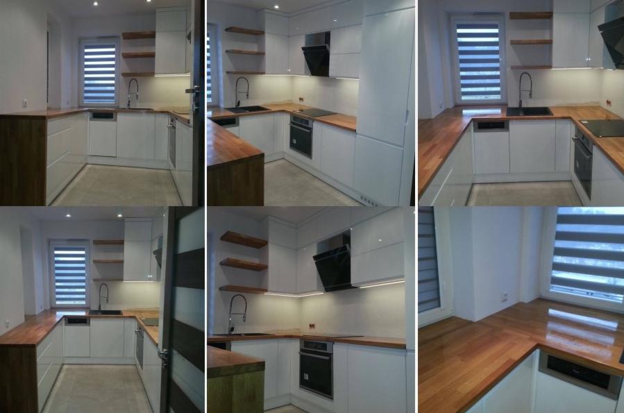 Nowoczesna, jasna kuchnia z białymi szafkami i drewnianymi blatami. Widoczne otwarte drewniane półki, czarny okap i rolety w oknie. Ujęcie z różnych perspektyw.