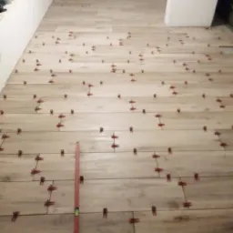 Układanie podłogi z płytek imitujących drewno, widoczne poziomica i krzyżyki dystansowe.