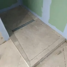 Płytki podłogowe w kabinie prysznicowej z odpływem liniowym, widoczne krzyżyki dystansowe i niedomalowane ściany.