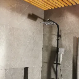 Wykończona kabina prysznicowa z szarą, marmurkową glazurą na ścianach, czarną armaturą i drewnianym, ażurowym sufitem. W ściennej wnęce widoczne narzędzia i ściereczka.