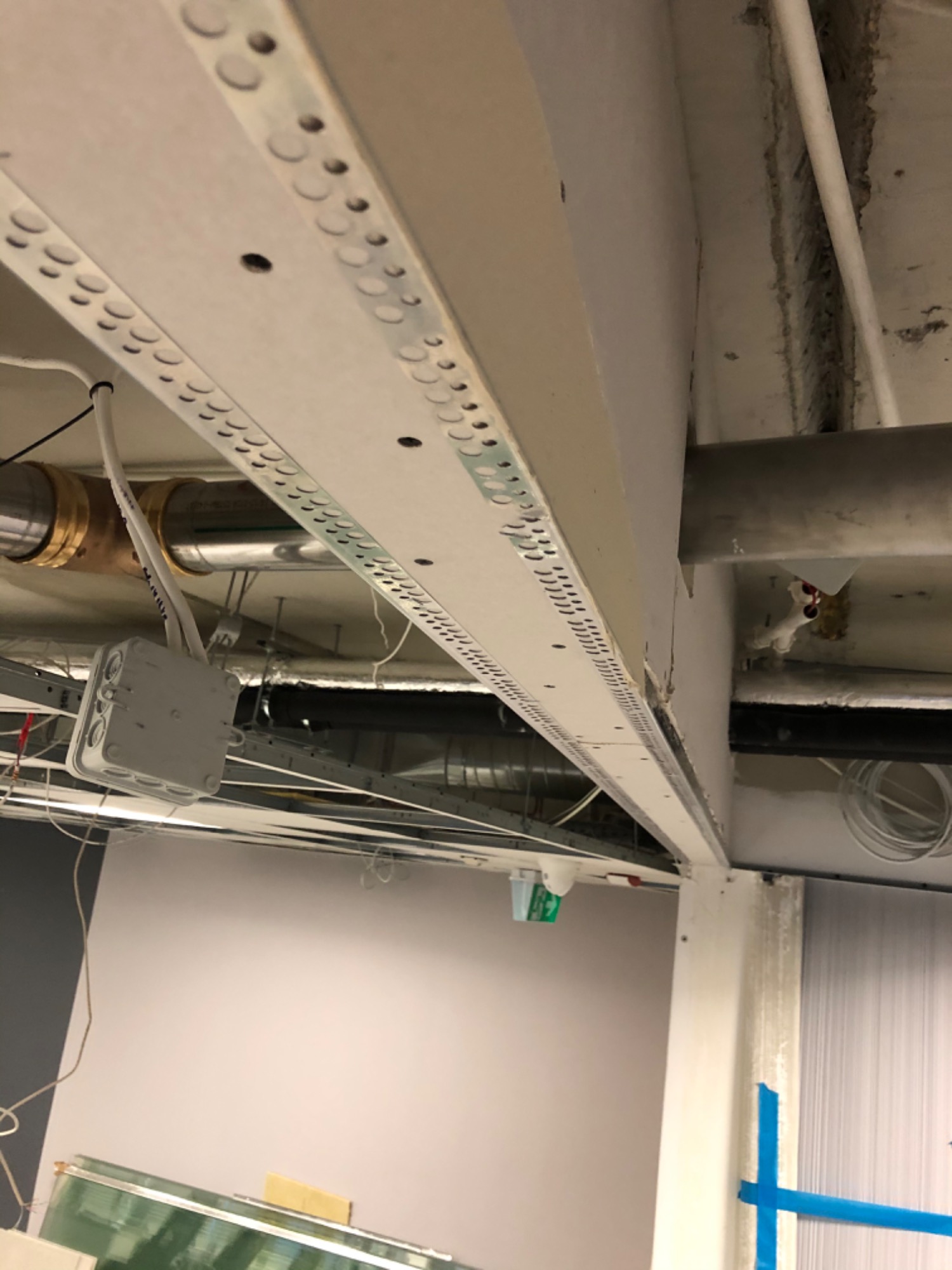 Montaż profili pod płytę gipsowo-kartonową na suficie w biurze, widoczne instalacje i rury pod stropem.