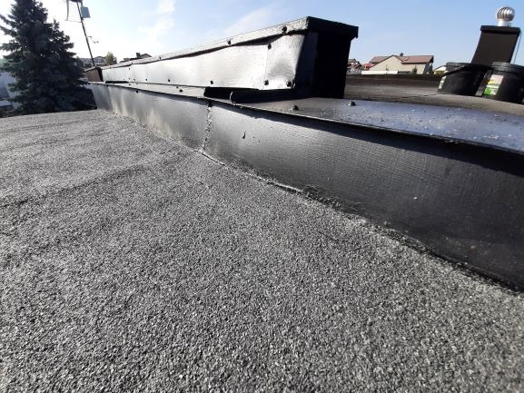 Szczegółowe ujęcie pokrycia dachu papą z obróbką blacharską, widoczne łączenia i elementy mocujące.