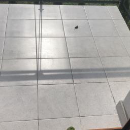 MarekProchal - Jasnoszare płytki gresowe na balkonie, widok z góry przez otwarte drzwi balkonowe, cień barierki, pojedynczy liść na płytkach.