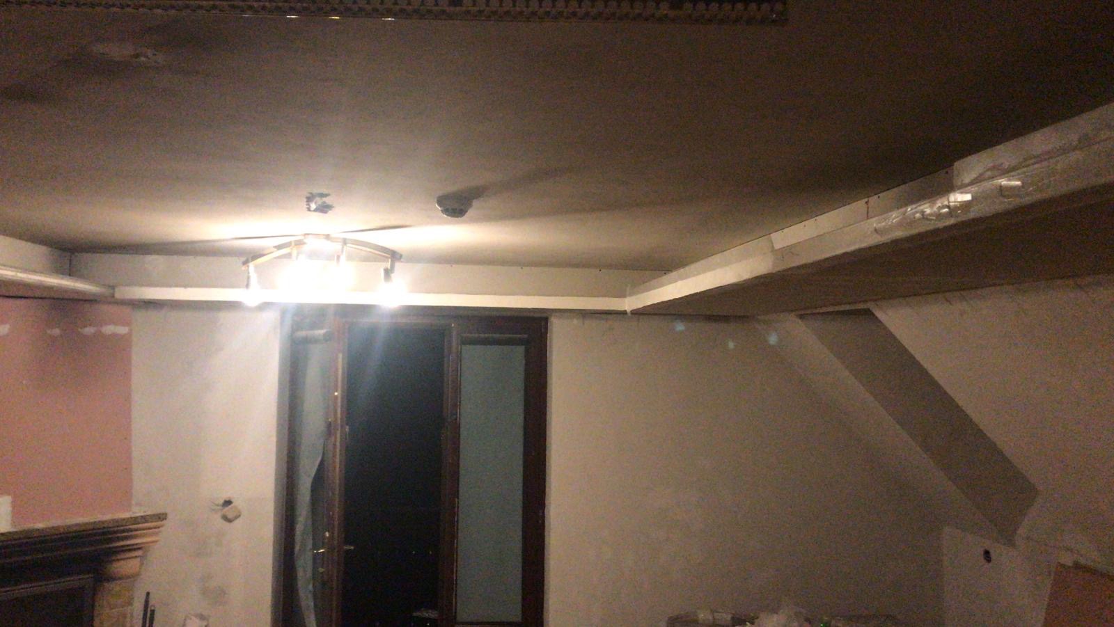 Widok na sufit z zamontowaną konstrukcją pod zabudowę LED, widoczne płyty karton-gips i częściowo pomalowane ściany w remontowanym pomieszczeniu.