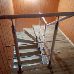 Schody wyłożone brązowymi płytkami imitującymi drewno, z metalowo-drewnianą balustradą i pomarańczową boazerią na ścianach.