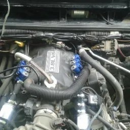 Silnik 3.8L V6 z elementami instalacji gazowej, widoczne niebieskie wtryskiwacze, przewody i filtry, w komorze silnika Jeepa Wrangler.