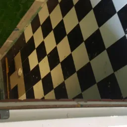 Ukończona podłoga w szachownicę z czarno-białych płytek, widoczne zielone płytki na ścianie i fragment wanny, ujęcie z góry.